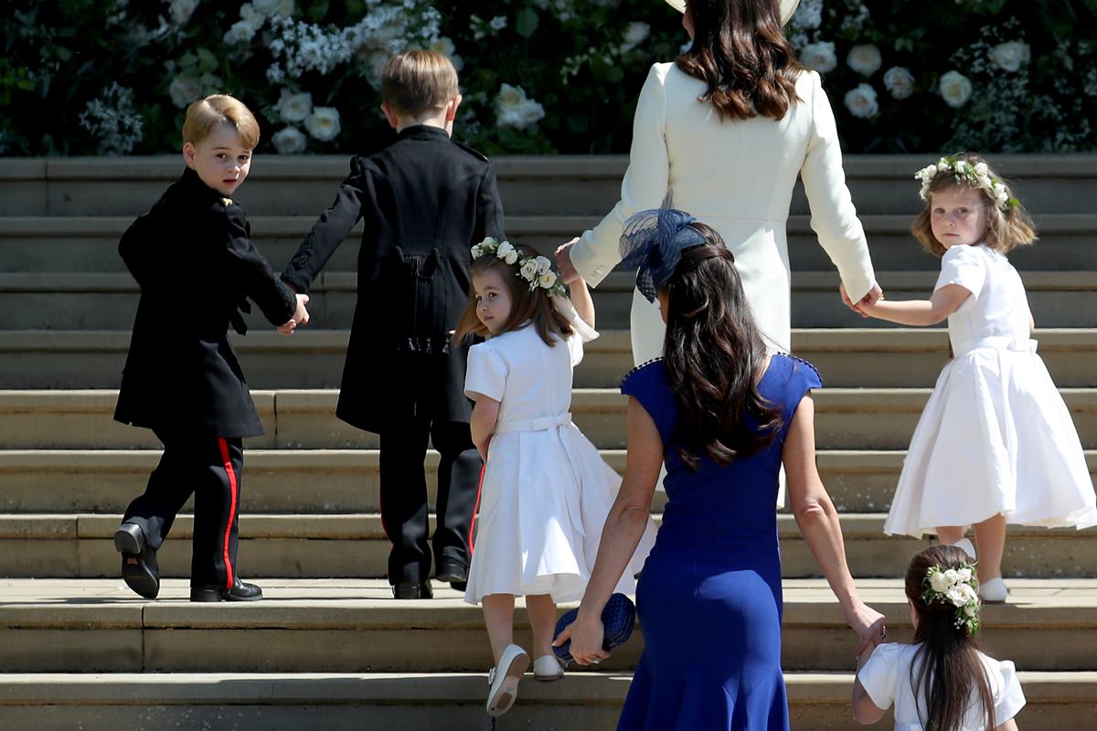 Foto colorida de meninos com trajes militares e meninas com roupas de damas de honra. Elas estão acompanhadas por mulheres enquanto sobem uma escadaria - Metrópoles