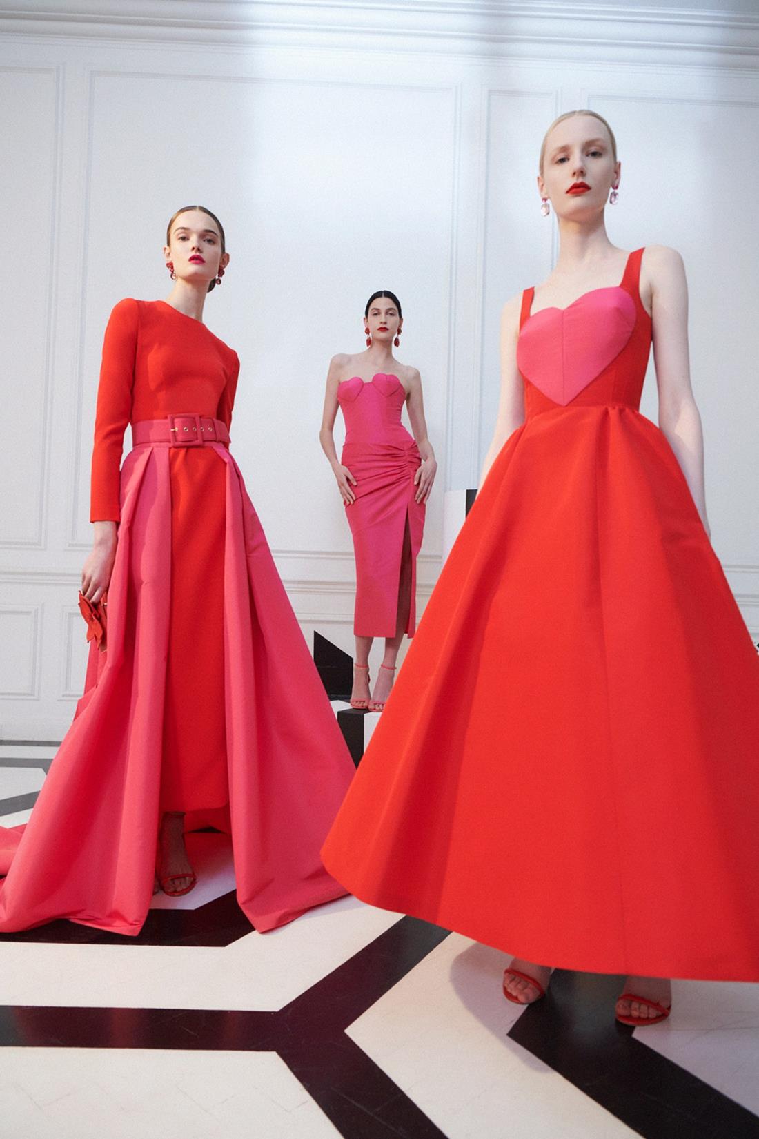 Três modelos brancas e jovens, de cabelo liso preso, posam para foto de campanha da marca Carolina Herrera. Elas usam vestidos vermelhos com detalhes em rosa. - Metrópoles