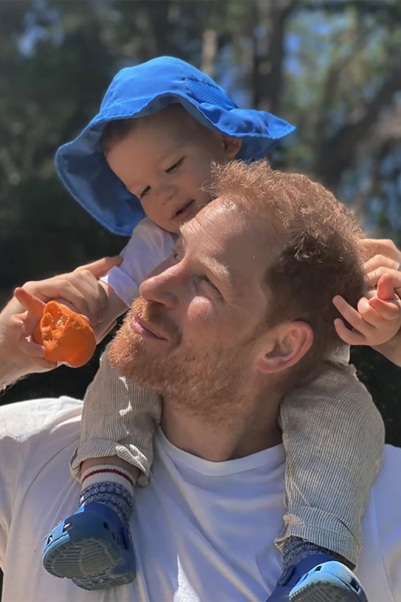 Foto colorida de menino de chapéu azul nas costas de homem branco, ruivo e com camiseta branca - Metrópoles