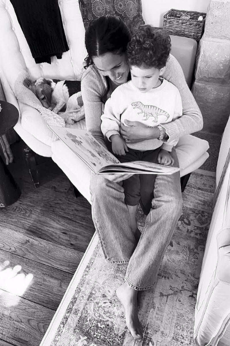 Foto em preto e branco de mulher com menino no colo segurando um livro. Eles estão sentados no chão - Metrópoles