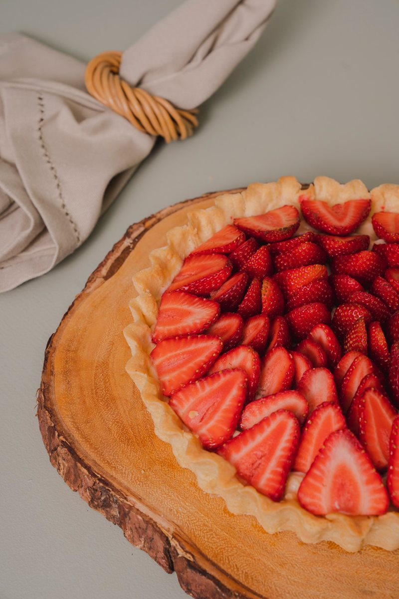 Foto colorida de torta com topo de morangos em uma bandeja de madeira - Metrópoles