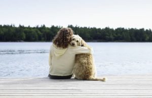 Foto colorida de mulher sentada na beira do pier abraçada com o cachorro - Metrópoles