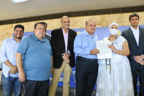 Mulher com roupa religiosa branca recebe documento em foto com homens de terno e roupa social