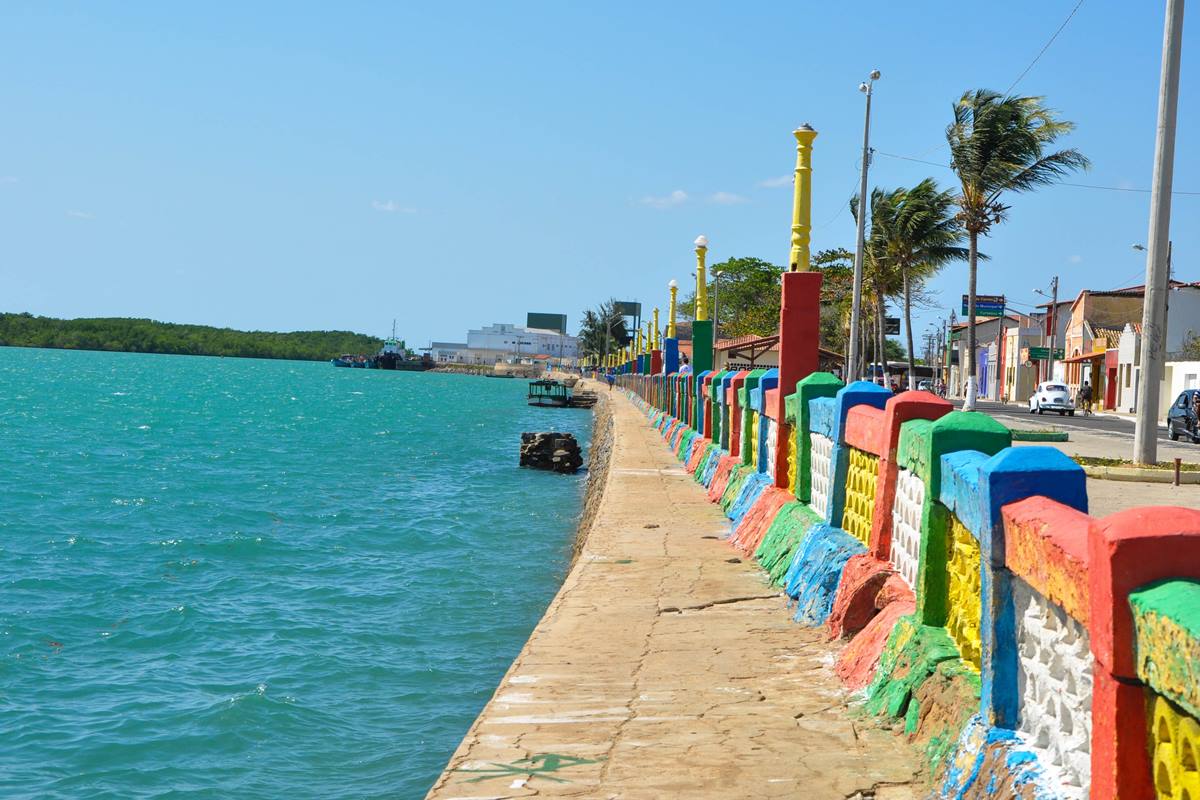 Foto colorida de mar rodeado por um muro pequeno pintado de várias cores - Metrópoles