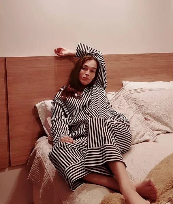 Camila Lente, dona da Beige, usando pijama listrado na cama - Metrópoles 