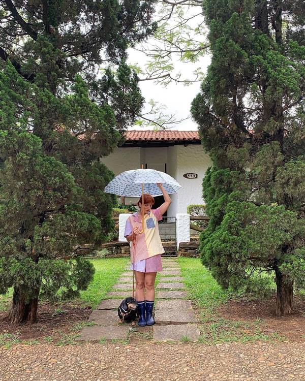 Dona da marca Maria Barbosa pijamas usa pijama colorido na frente de uma casa com o guarda-chuva na mão - Metrópoles 