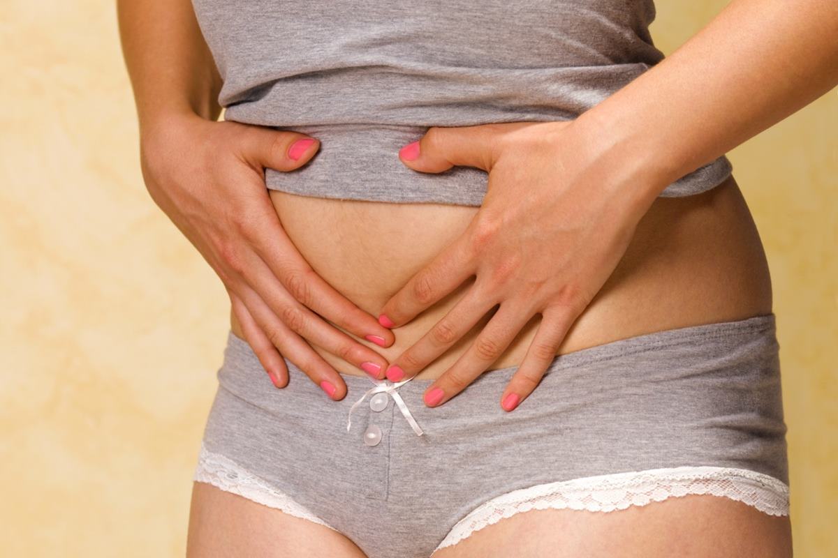 Foto colorida de mulher com as mãos na barriga