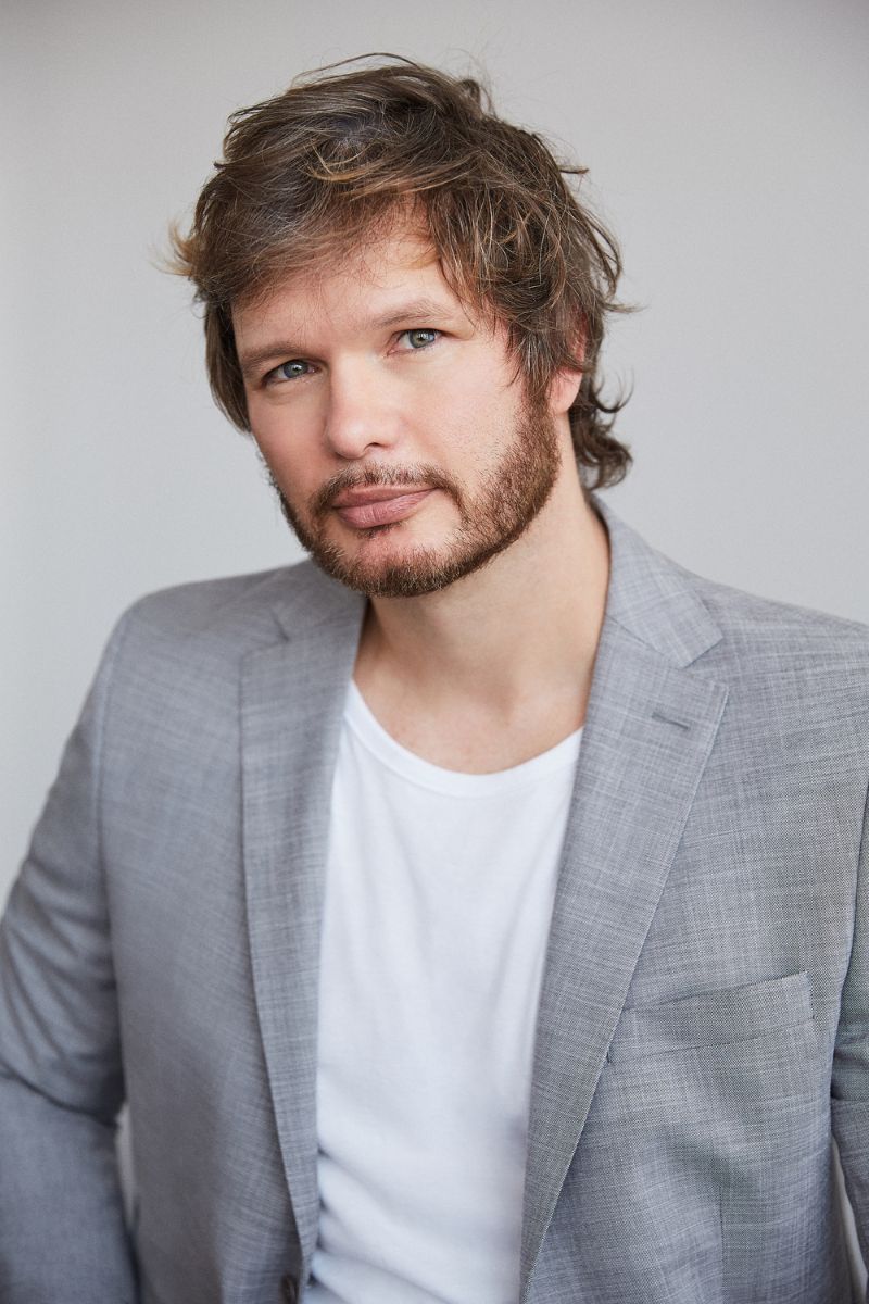 Foto colorida de homem branco e com barba vestido com blazer cinza e blusa branca - Metrópoles