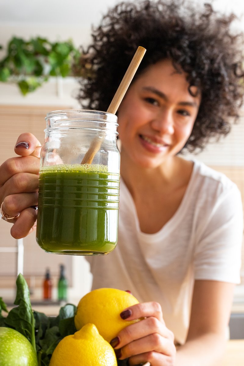 Foto colorida de mulher parda segurando copo de suco verde com canudo - Metrópoles