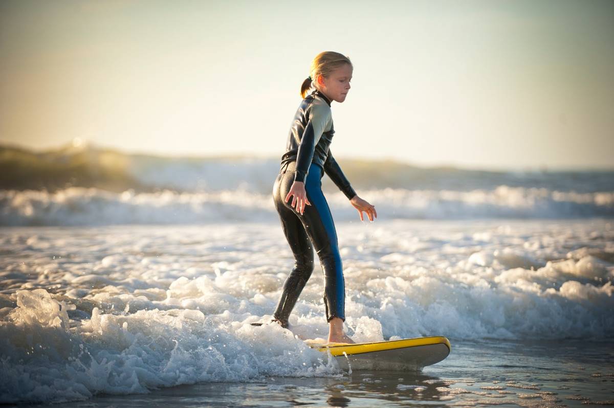 Foto colorida de menina e cima de uma prancha surfando