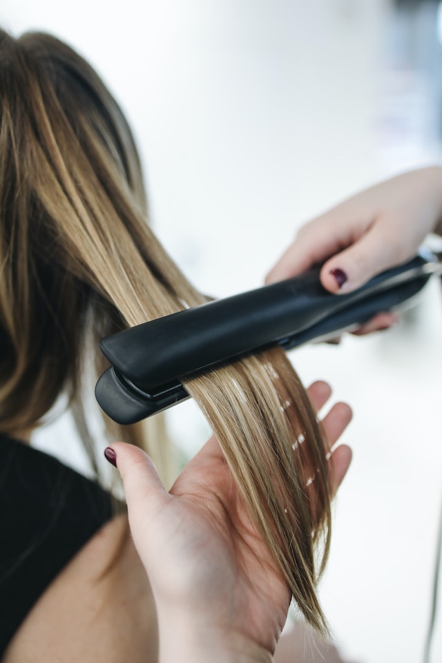 Dedos passando chapinha em cabelo loiro de mulher - Metrópoles