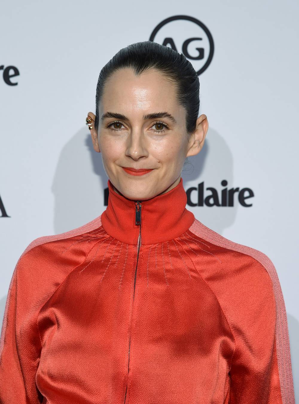 A stylist Karla Welch, uma mulher branca e jovem, de cabelo liso preto, posa para foto em evento da revista Marie Claire em 2018. Ela usa um casaco com gola alta na cor vermelha. - Metrópoles