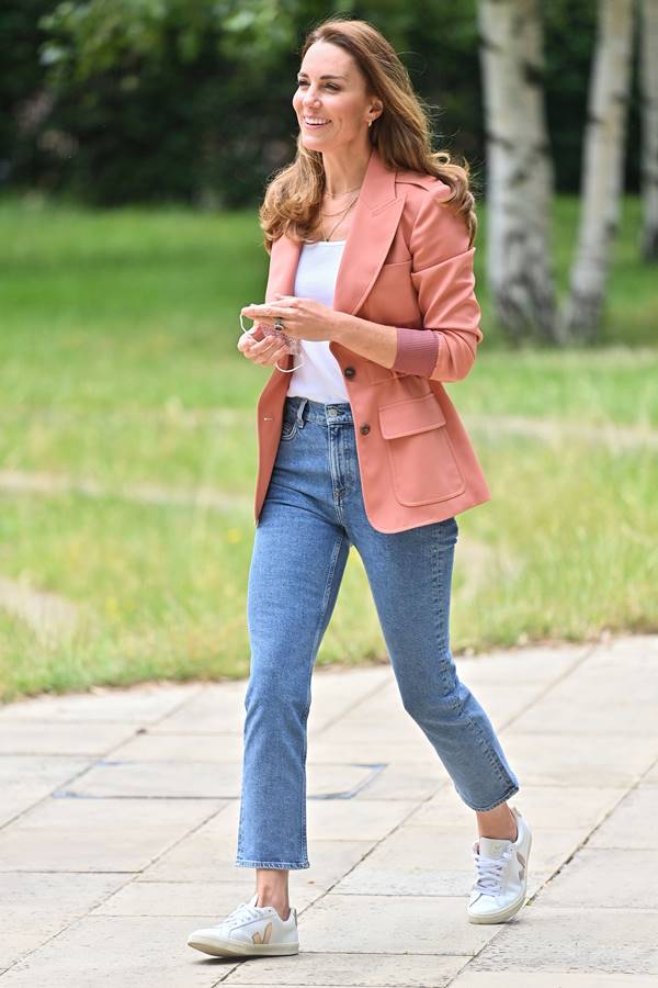 Mulher branca ando em calçada. Ela está usando par de calças jeans e blazer branco - Metrópoles