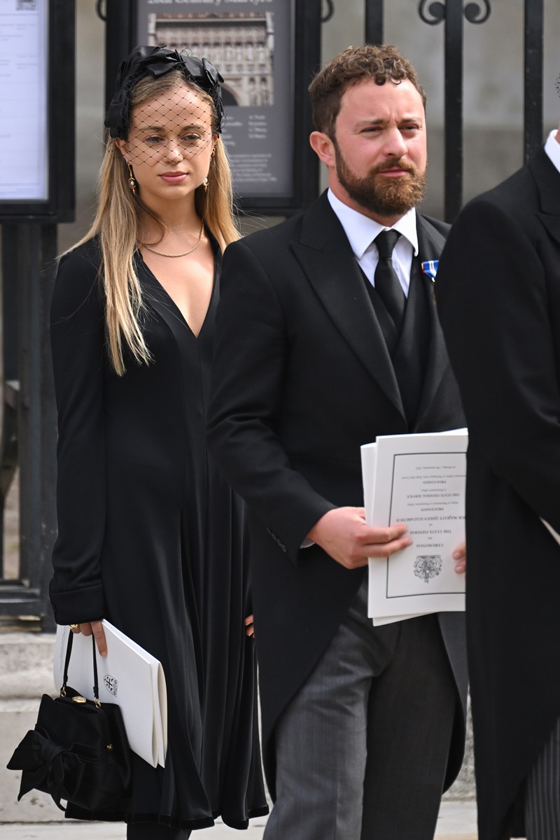 Foto colorida de mulher branca e loira vestida de preto ao lado de homem branco, barbudo e com terno - Metrópoles