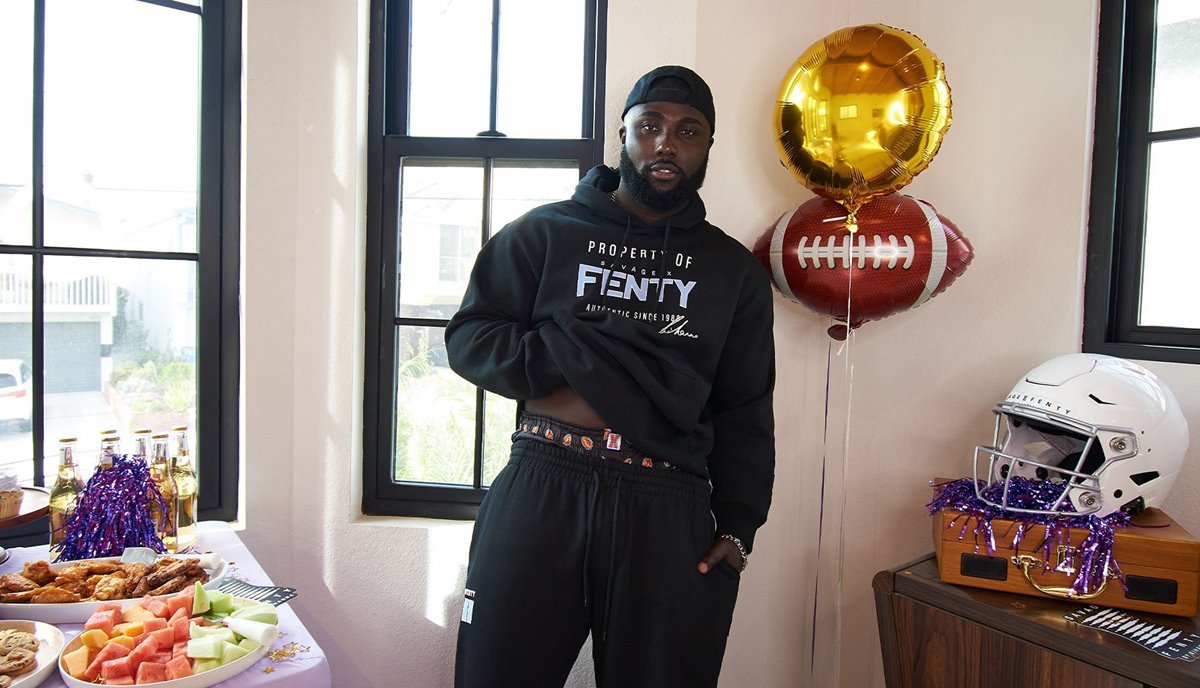 Campanha de divulgação da Game Day, coleção da marca Savage X Fenty em referência ao evento Super Bowl. A marca de lingeries é da cantora Rihanna. Na imagem, modelo homem, jovem e negro usa roupas da marca: um conjunto de casaco e calça de moletons pretos. - Metrópoles