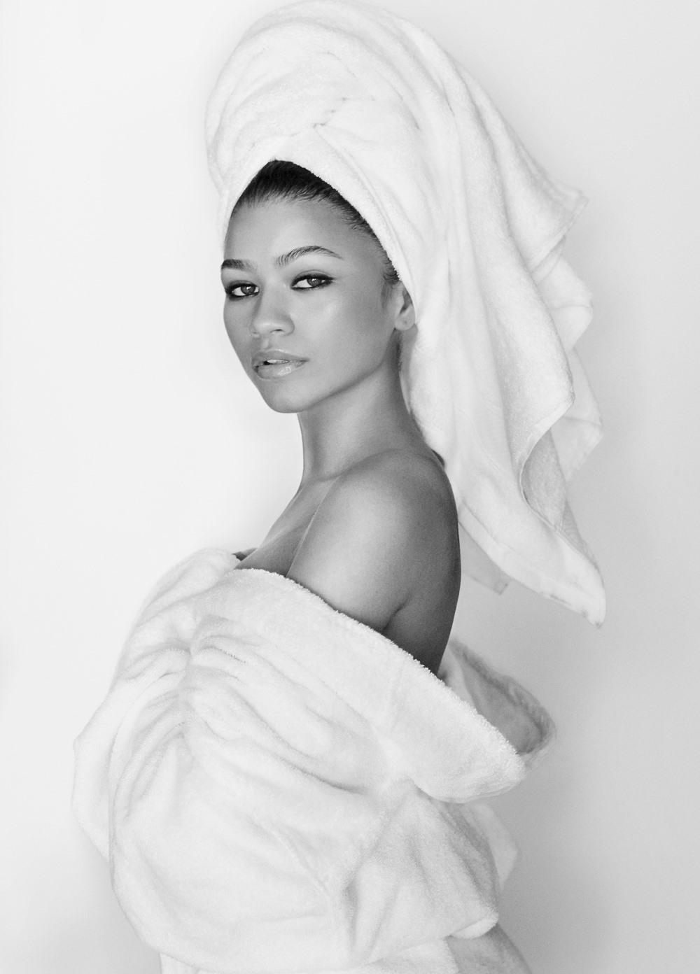 A atriz Zendaya, uma mulher negra jovem, com cabelos ondulados castanhos, posa em um fundo branco seminua. A foto faz parte do projeto Towel Series, do fotógrafo Mario Testino. Nessa série, os personagens aparecem tampando parte do corpo apenas com toalhas brancas. - Metrópoles