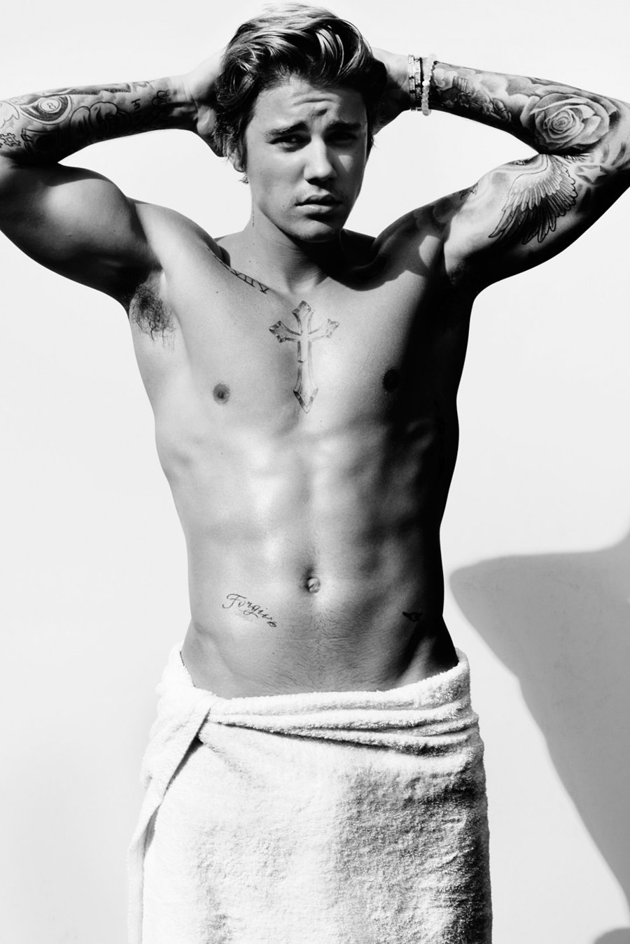 O cantor Justin Bieber, um homem jovem e branco, de cabelos lisos e louros, posa em um fundo branco seminua. A foto faz parte do projeto Towel Series, do fotógrafo Mario Testino. Nessa série, os personagens aparecem tampando parte do corpo apenas com toalhas brancas. - Metrópoles