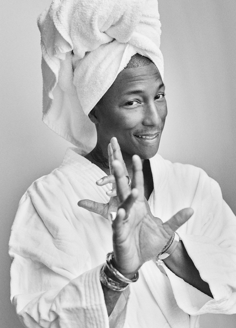 O cantor Pharrell Williams, homem negro e de meia idade, com cabelo raspado, posa para foto em um fundo branco seminu. A foto faz parte do projeto Towel Series, do fotógrafo Mario Testino. Nessa série, os personagens aparecem tampando parte do corpo apenas com toalhas brancas. - Metrópoles