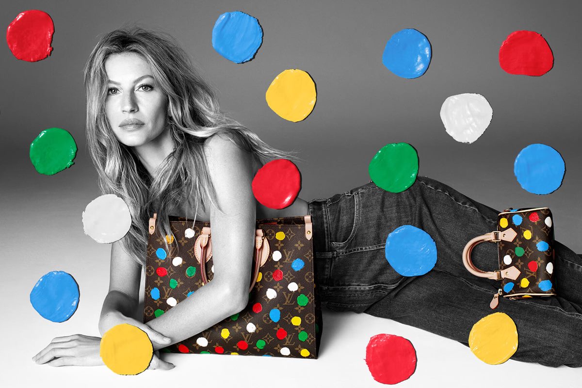 A modelo Gisele Bündchen, uma mulher branca e de meia idade, com cabelo liso loiro, posa para campanha da marca Louis Vuitton. Ela usa uma calça jeans e tampa a região dos seios com uma bolsa da marca. - Metrópoles