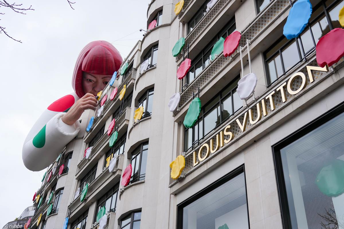 Fachada de uma loja da grife Louis Vuitton. Várias bolas coloridas que simulam tintas coloridas estão espalhadas pelo prédio. No teto, tem um balão inflável que imita a artista plástica Yayoi Kusama, uma idosa japonesa de cabelos curtos vermelhos. - Metrópoles