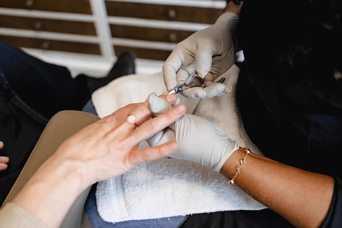 Mãos de uma mulher branca e jovem na manicure. A profissional retira as cutículas das unhas com um alicate. - Metrópoles