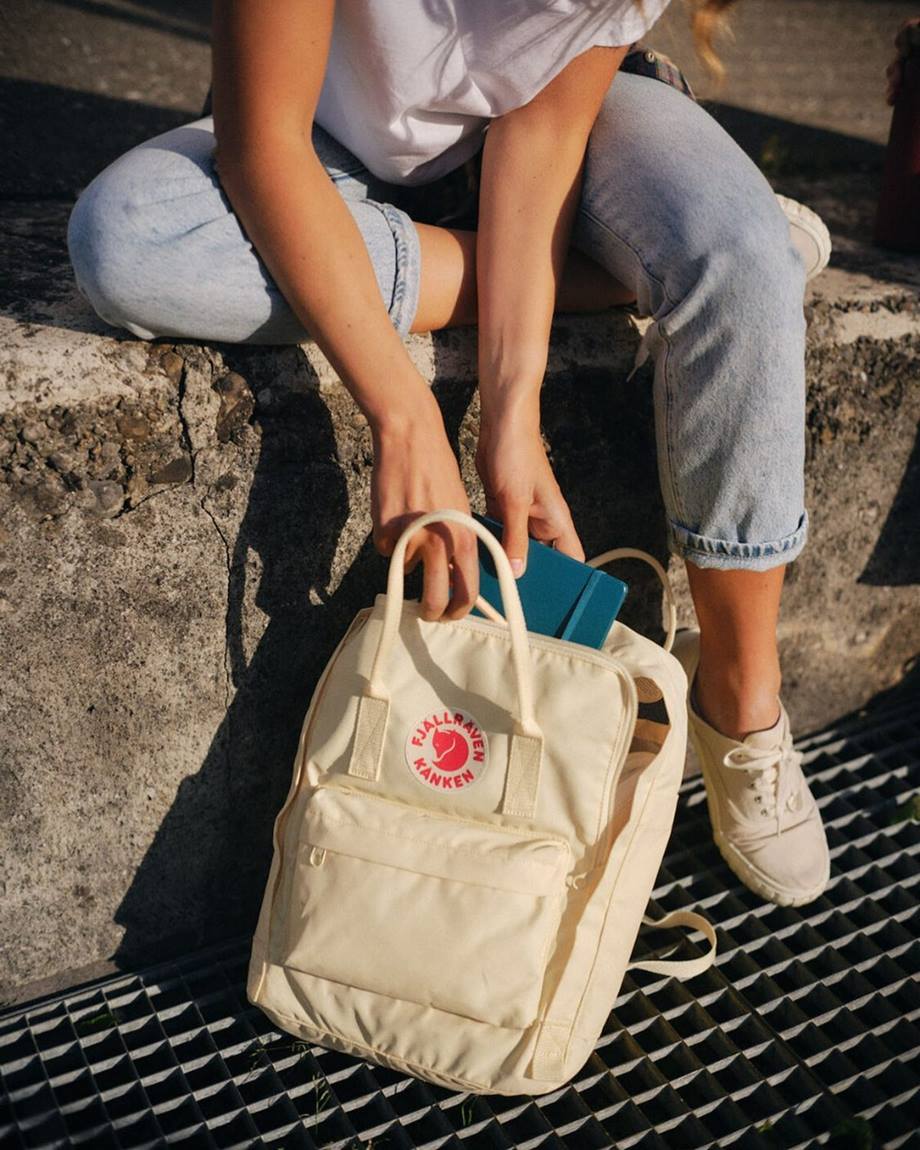 Mulher branca e jovem mexendo em uma mochila branca da marca Fjällräven. Não é possível ver seu rosto na foto. Ela usa uma camiseta branca, uma calça jeans e um tênis também branco. - Metrópoles