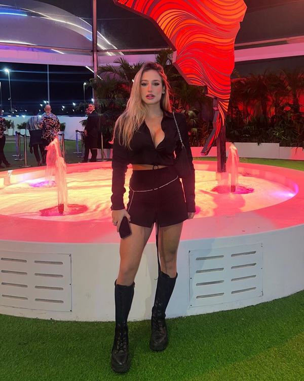 Mulher branca em evento. Ela está posando para a foto com roupas pretas - Metrópoles