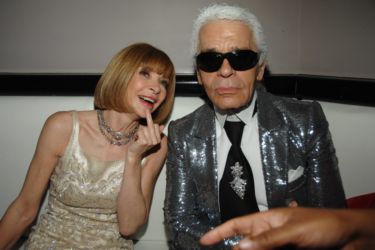 O estilista Karl Lagerfeld, um homem branco e idoso, de cabelos grisalhos, ao lado da jornalsita Anna Wintour. Ela é uma mulher branca e de meia idade, de cabelo curto liso e loiro. - Metrópoles