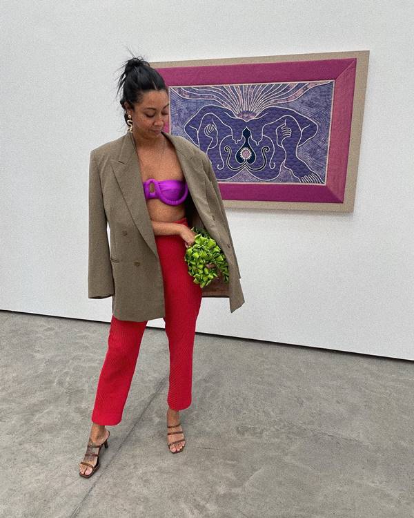 Mulher negra usa top roxo, calça vermelha, blazer e sandália de salto - Metrópoles 