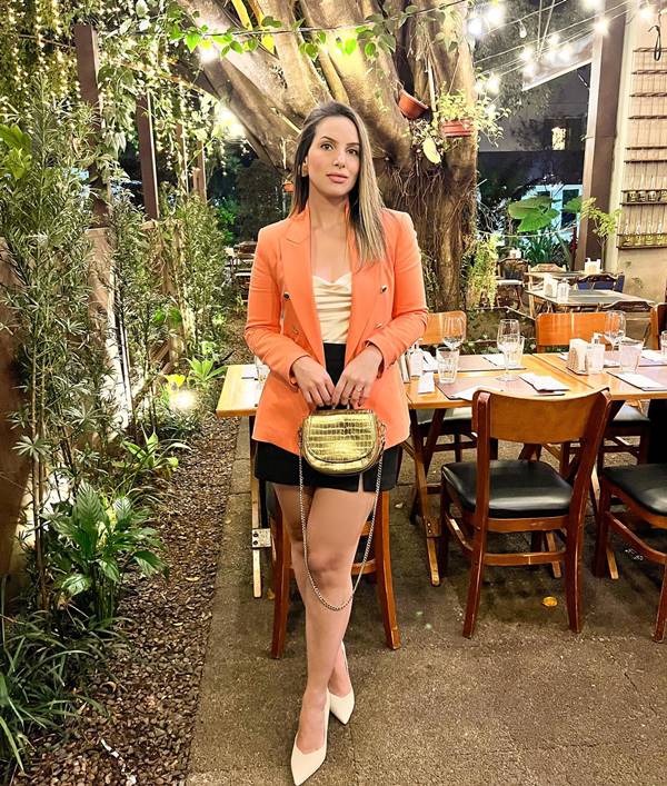 Mulher branca usa blazer laranja, camisa branca, saia preta e sapato - Metrópoles 