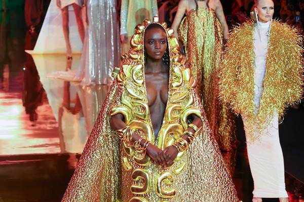 Mulher negra vestida com capa dourada em desfile de moda na passarela - Metrópoles 