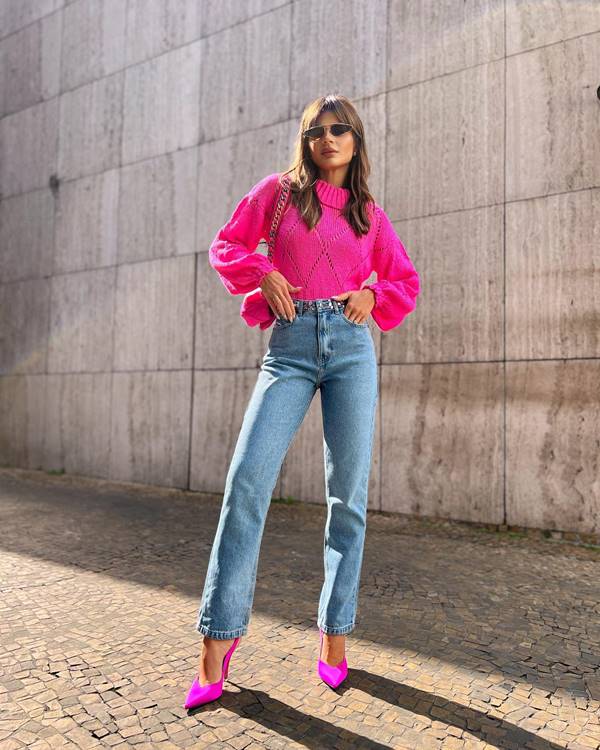 mulher branca usa óculos de sol, blusa de manga longa rosa, calça jeans e salto rosa - Metrópoles 