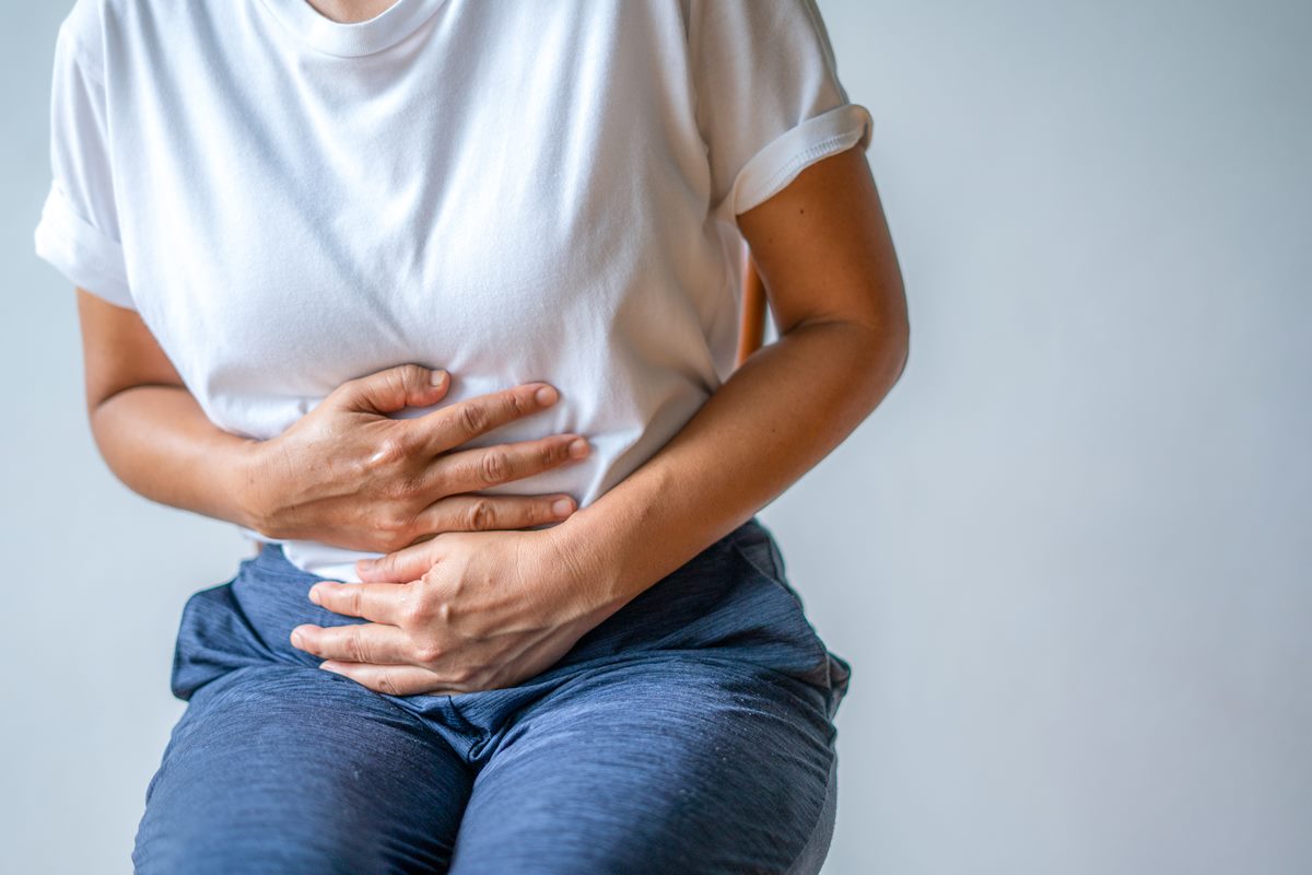 Imagem de mulher de camisa branca e calça azul segurando a barriga com as duas mãos - Metrópoles