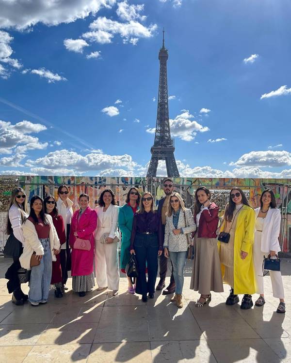 Grupo de pessoas em frente a Torre Eiffel, em Paris, ao fundo céu azul - Metrópole