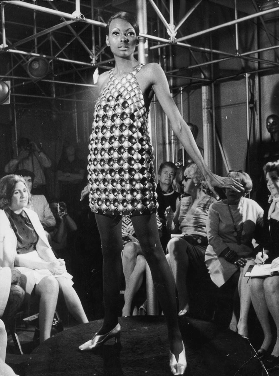 Modelo jovem e negra em um desfile. Ela usa um vestido mini, de bolas prateadas, na passarela. O desfile é da marca Paco Rabanne. A foto é de 1968. - Metrópoles