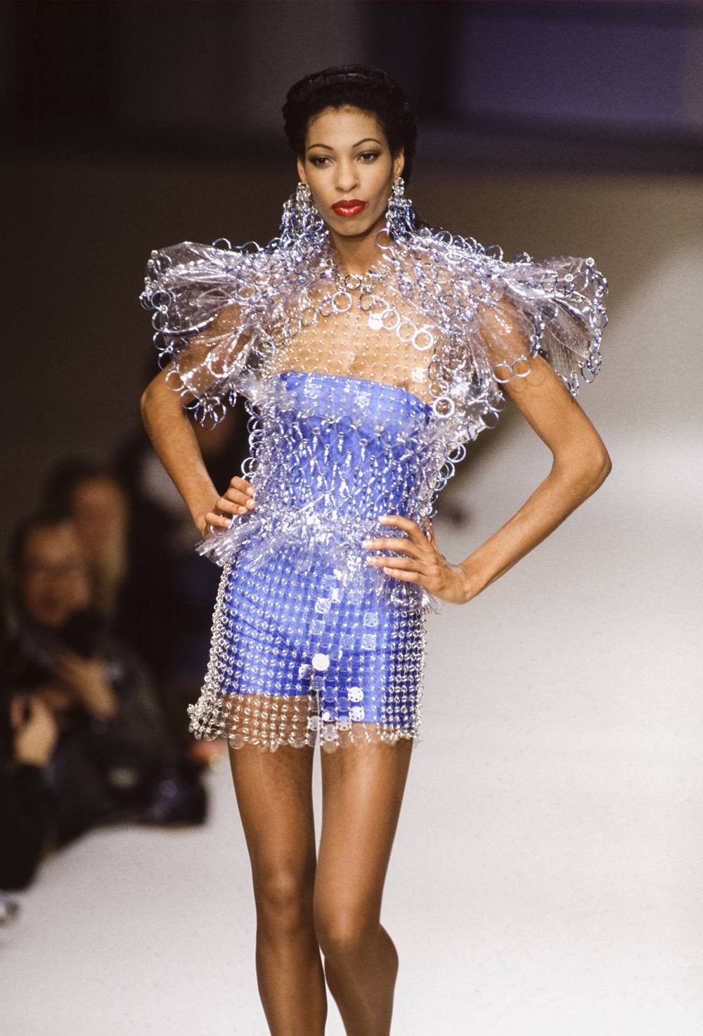 Modelo jovem e negra em um desfile. Ela usa um vestido azul com uma estrutura metalizada por cima, na passarela. O desfile é da marca Paco Rabanne. A foto é de 1994. - Metrópoles