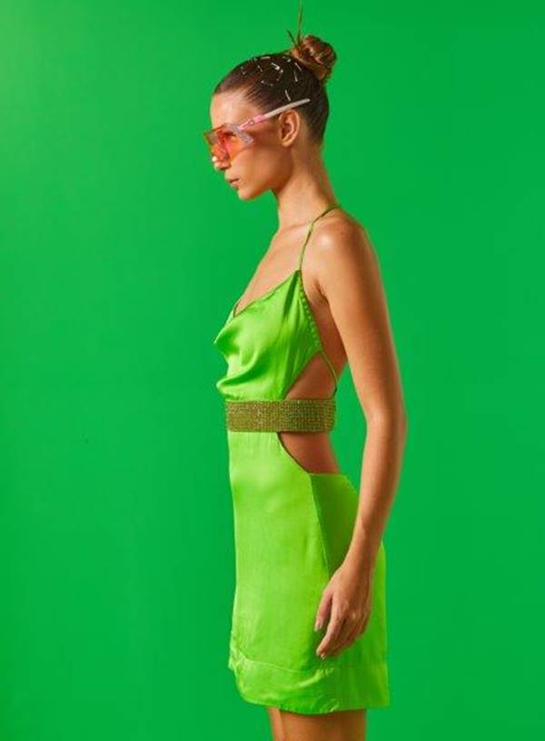 De lado, modelo branca usa vestido verde acetinado com faixa de brilho abaixo do peito - Metrópoles