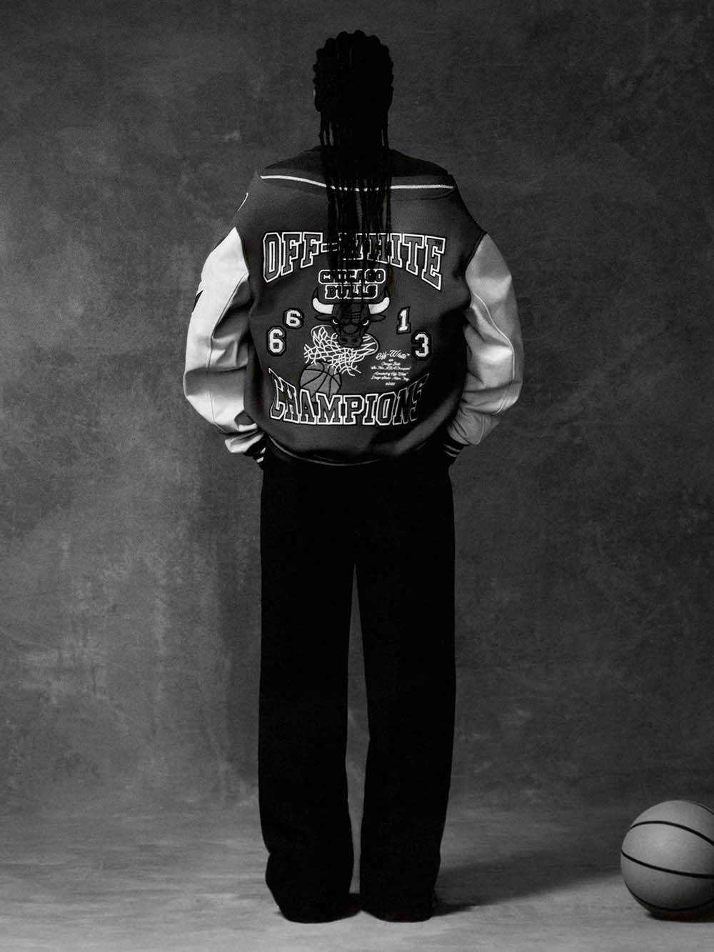 Campanha de divulgação da coleção de roupas da marca Off-White com o time de basquete Chicago Bulls. Na imagem, é possível ver uma mulher negra e jovem, de cabelos trançado, usando calça e uma camiseta e, por cima, uma jaqueta esportiva com o touro do Chicago Bulls estampado. - Metrópoles