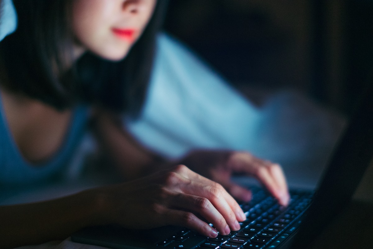 Foto colorida de mulher branca em ambiente escuro usando um notebook - Metrópoles