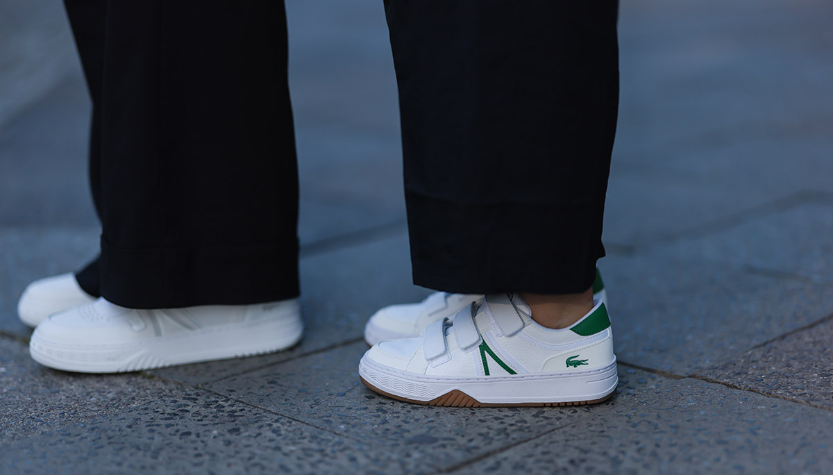 Pessoa na rua usando uma calça preta folgada e um tênis branco, de couro, da marca Lacoste. - Metrópoles