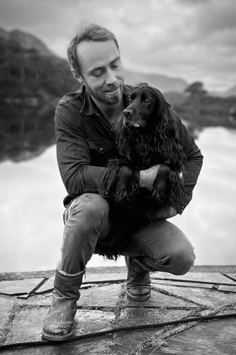 Foto em preto e branco de homem segurando no colo um cachorro. O homem está abaixado - Metrópoles