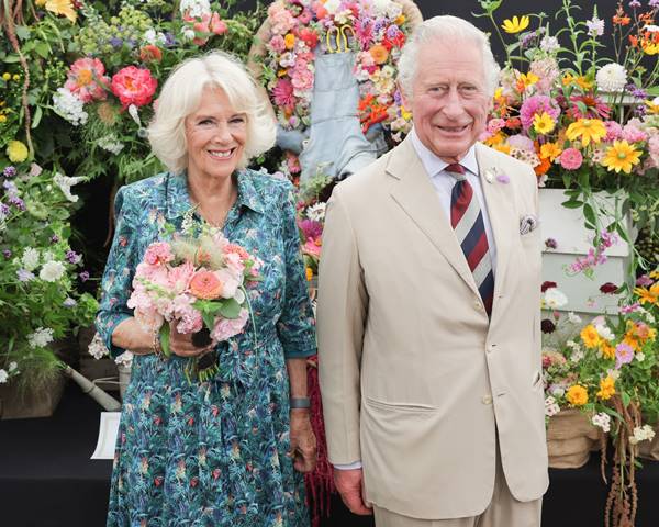 Casal andando em cerimônia. Os dois estão de braços dados e a mulher está segurando um buquê de flores - Metrópoles