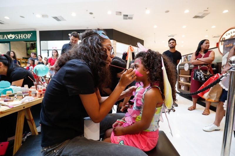 Foto de uma criança em um shopping fazendo uma pintura facial e infantil no rosto