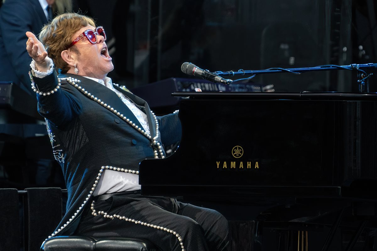 Foto colorida de homem branco, vestido com terno com brilhos, tocando piano - Metrópoles