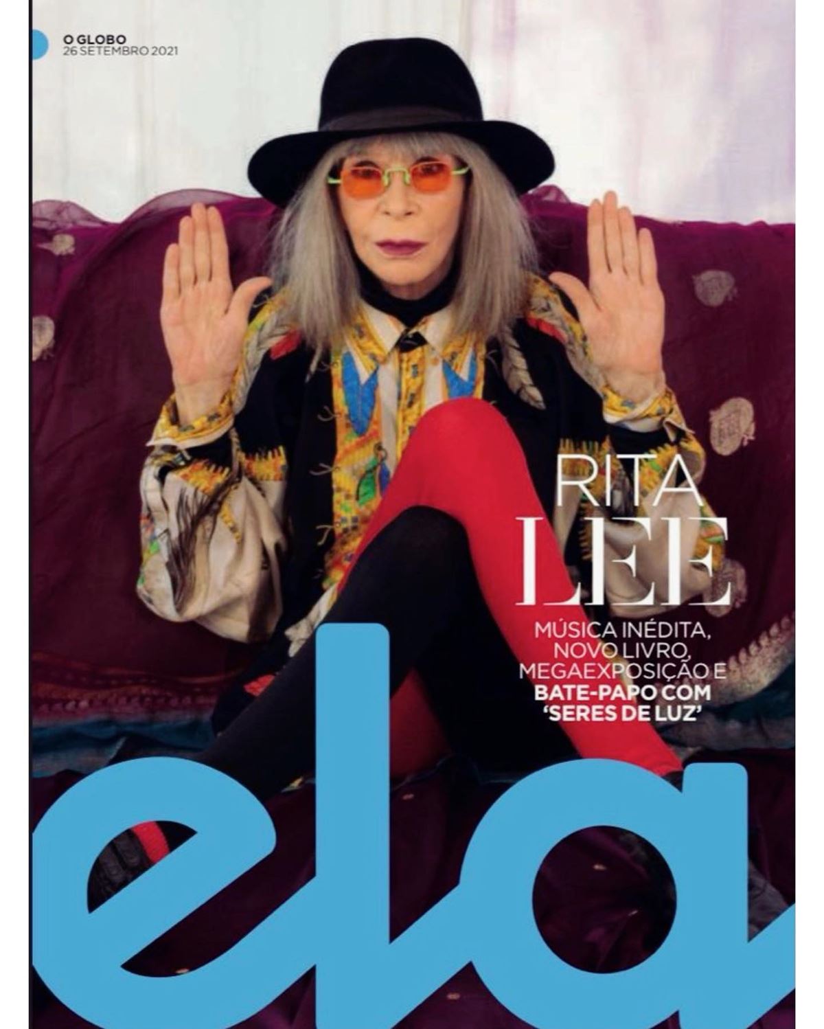 A cantora Rita Lee, uma mulher branca e idosa, na capa do caderno Ela, do jornal O Globo. Ela usa uma meia calça vermelha, um vestido preto com detalhes brancos, um óculos laranja e um chapéu preto. - Metrópoles