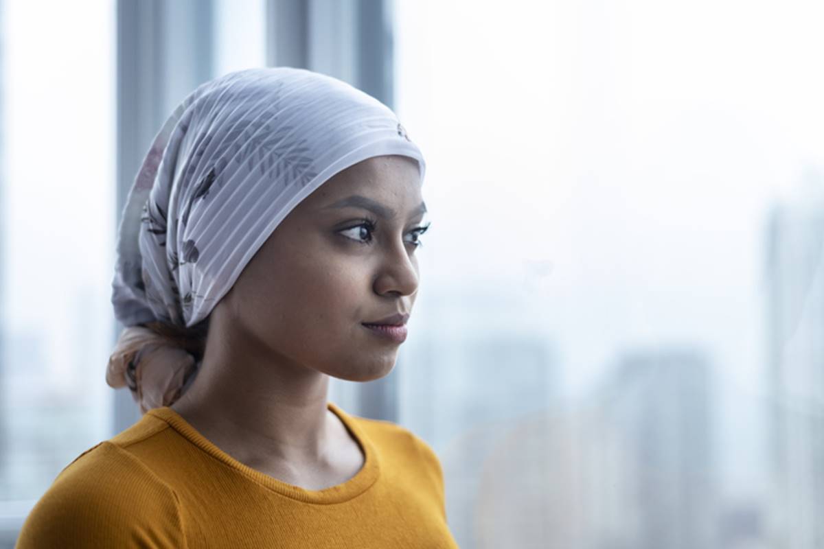 Mulher jovem com lenço na cabeça olhando pela janela - Metrópoles