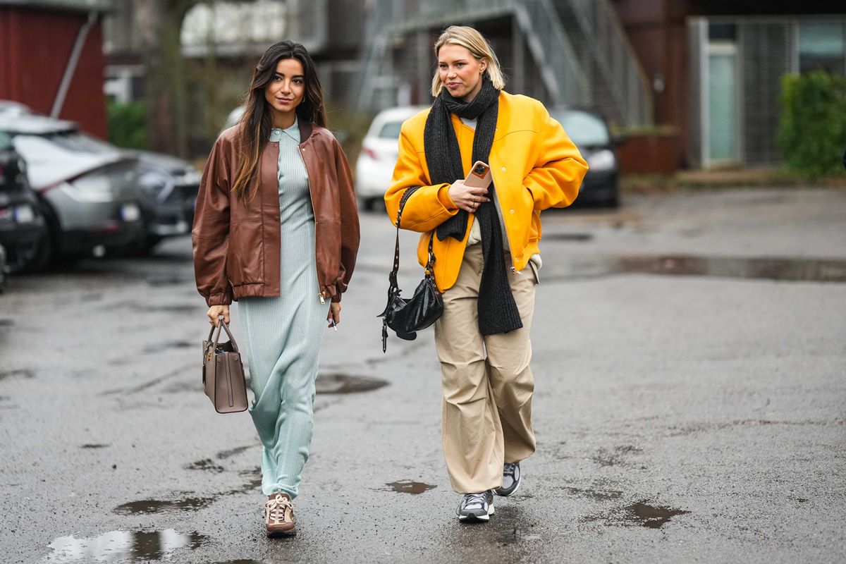 Duas amigas jovens e brancas andam pela rua. Uma tem o cabelo castanho longo e liso e a outra é loira, com o cabelo em um corte chanel. Elas usam roupas de frio e tênis. - Metrópoles