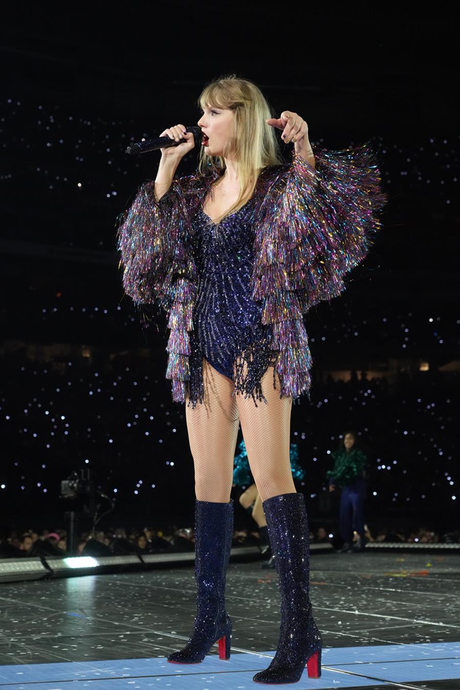 A cantora Taylor Swift, uma mulher jovem e branca, de cabelo loiro liso. Ela está no palco, na turnê The Eras Tour, e usa um body preto com brilhos, da Oscar de La Renta, e um bota preta da Louboutin. - Metrópoles