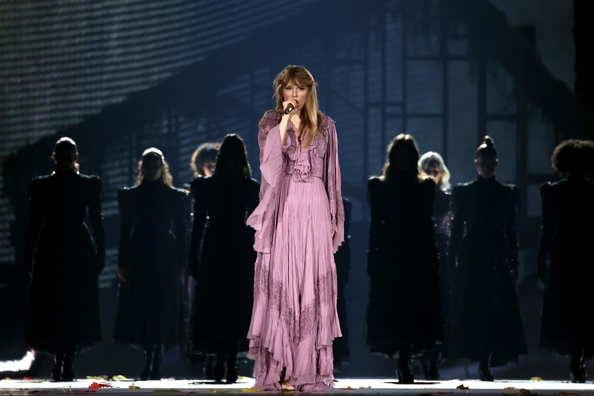 A cantora Taylor Swift, uma mulher jovem e branca, de cabelo loiro liso. Ela está no palco, na turnê The Eras Tour, e usa um vestido roxo com babados e camadas da estilista Alberta Ferretti. - Metrópoles