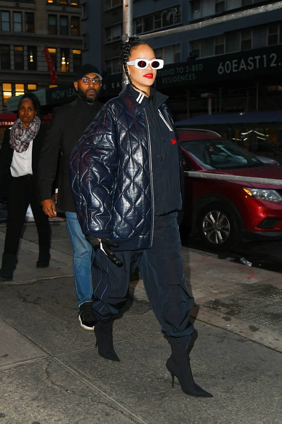 A cantora Rihanna, uma mulher negra e jovem, com o cabelo preto penteado em uma trança, andando pelas ruas de Nova York. Ela usa um look todo preto: casaco, jaqueta bomber do couro, calça, bota de salto. O óculos escuros, por sua vez, tem uma armação branca. - Metrópoles